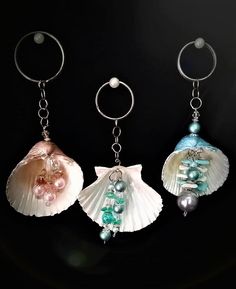 three seashells with pearls are hanging from key chains on a black background,