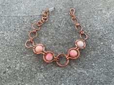 The Pink Nest Bracelet features polished agate stones in rich pink and cream hues with flecks of yellow and orange, wrapped in high-quality pure copper.  Flaunt this modern, art-deco-inspired look with a sophisticated feel to compliment your style and elevate any outfit. Give as a memorable unique gift to the favorite woman in your life: For Mother's Day, anniversary presents, Christmas gifts, birthday gifts, graduation and bachelorette parties. ## Sizing Total length is 7.5 inches. ## Materials Every item is 100% handmade and one-of-a-kind. The wire-wrapped raw copper jewelry is oxidized and polished to beautifully highlight details of the wirework. Finally, it's sealed with a protective clear coat to prevent tarnishing and allergic reactions. Since gemstones are unique, a slight variatio Pink Rose Quartz Wire Wrapped Jewelry, Handmade Copper Wire Bangle Bracelet, Handmade Rose Gold Bracelets With Round Beads, Handmade Rose Gold Bracelet With Round Beads, Adjustable Rose Gold Wire Wrapped Bracelets, Pink Opal Bracelet Jewelry, Handmade Rose Quartz Jewelry In Rose Gold, Handmade Agate Bangle Jewelry, Adjustable Pink Opal Bracelet