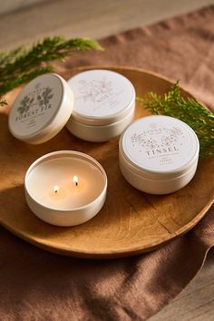 three white candles sitting on top of a wooden plate next to some greenery and pine branches