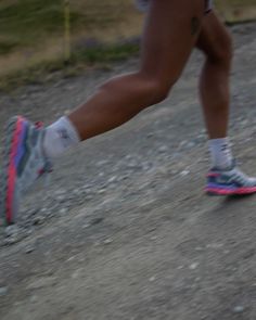 a close up of a person's running shoes on a dirt road with grass and bushes in the background