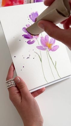 a woman is painting flowers on a piece of white paper with purple paint and a pair of scissors