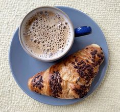 a blue plate topped with a croissant and a cup of coffee