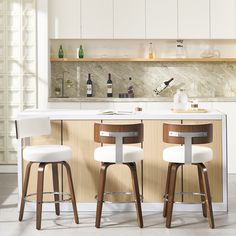 two white stools sit in front of an island with wine bottles on the shelves