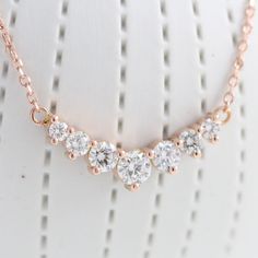 This timelessly gorgeous diamond necklace showcases brilliant white diamonds set in a lustrous 14k rose gold curved 7 stone pendant setting creating an eye-catching and chic look. The 7 diamond pendant hangs gorgeously from a solid 14k rose gold cable chain. The length of the gold chain can be adjusted to either 16" or 18" long to suit your style! This curved diamond necklace matches perfectly with our seven diamond wedding band and earrings. It can be made in your choice of white, rose, or yell 14k Rose Gold Anniversary Necklaces, 14k Rose Gold Necklace For Anniversary, Dazzling Rose Gold Diamond Necklace With Accents, Dazzling Rose Gold Necklace With Prong Setting, Dazzling Rose Gold Diamond Accents Necklace, Rose Gold Diamond Necklace With Prong Setting, Rose Gold Diamond Necklace For Anniversary, Dazzling Rose Gold Necklace With Cubic Zirconia, Dazzling Rose Gold Diamond Necklace