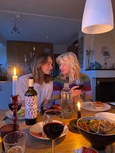 two women sitting at a table with wine and food