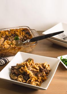 a plate of pasta with meat and vegetables on the side next to a casserole dish