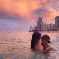 a man and woman are in the ocean with buildings in the backgrouds