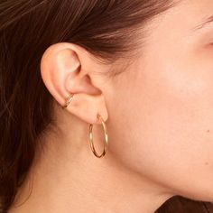 A woman wears her long brown hair tucked behind her ear. She wears one large gold hoop and a tiny gold ear cuff. Classic Clip-on Huggie Earrings For Everyday, Classic Everyday Clip-on Huggie Earrings, Everyday Yellow Gold Clip-on Huggie Earrings, Everyday Yellow Gold Clip-on Hoop Earrings, Yellow Gold Single Wrap Earring For Everyday, Modern Clip-on Hoop Earrings For Everyday, Everyday Yellow Gold Wrap Earrings, Classic Gold Wrap Earrings For Everyday, Catbird Jewelry