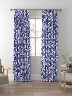 a blue and white curtain hanging in front of a window next to a wooden chair