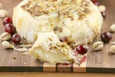 a piece of cheese with nuts and cranberries on a cutting board