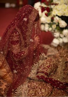 a woman wearing a red veil sitting on top of a bed covered in gold and white flowers