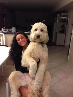 a woman is holding a large dog in her arms while sitting on a chair at the kitchen table