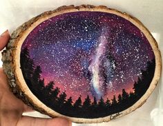 a person holding up a piece of wood with a painting on it that looks like the night sky