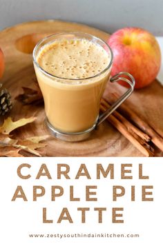 caramel apple pie latte on a wooden tray with apples and cinnamon sticks in the background