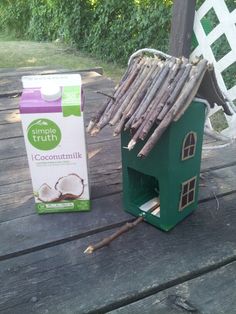 a green bird house next to a carton of coconut milk on a wooden deck