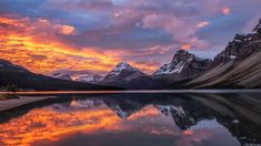 the sun is setting over mountains and water in this beautiful scene, with clouds reflected in the lake