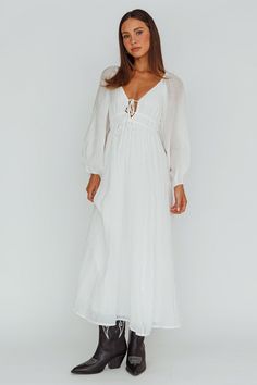 a woman wearing a white dress and cowboy boots, standing in front of a white background