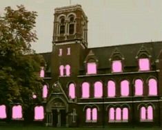 an old building with pink lights on the front and side windows, in front of some trees