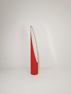 a red and white vase sitting on top of a white floor next to a wall