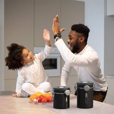 a man and woman sitting on the kitchen counter high fiving each other's hands