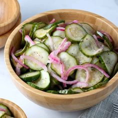 a wooden bowl filled with sliced cucumbers and onions next to two smaller bowls