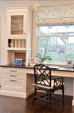 a desk and chair in a room with white cabinets, windows, and wood floors