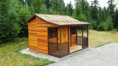 a small wooden shed sitting on top of a grass covered field in front of trees