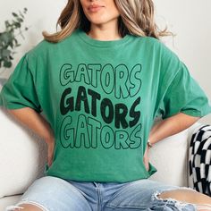 Gators Mascot Grunge Stacked Tee Light Green shown, but choose your color from the dropdown!  Each shirt is printed in-house by me using high-quality materials on a Comfort Colors shirt, which is the hottest style right now!  Available in unisex sizes S to 3X, and youth sizes, we've got you covered regardless of your preferred fit. Please note that ivory is ONLY available in Adult sizes!  Note: As each shirt is individually printed, slight variations in color and placement may occur, adding to t Green T-shirt With Letter Print For Fans, Green Letter Print T-shirt For Fan Gear, Casual Green Sublimation T-shirt With Team Name, Green Graphic Print T-shirt For Fan Gear, Relaxed Fit T-shirt With Screen Print For Fan Gear, Relaxed Fit T-shirt With Screen Print For Fans, Green Team Spirit Tops With Sublimation Print, Green Fan Apparel T-shirt For Game Day, Relaxed Fit Sports Fan Graphic Tee