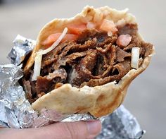 a hand is holding a sandwich with meat and onions on it, wrapped in tin foil