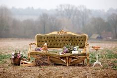 a couch sitting in the middle of a field next to a table with flowers on it