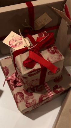 two wrapped presents sitting on top of each other with red ribbons and tags attached to them