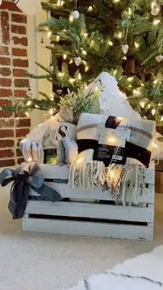 a christmas tree is decorated with white and black ribbons, lights, and presents in a wooden crate