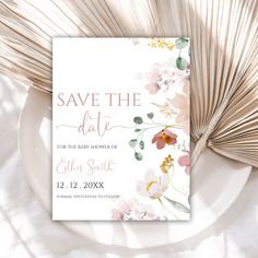 save the date card on a plate with flowers and palm fronds next to it