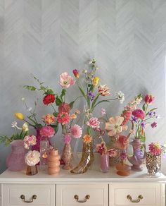 a white dresser topped with lots of vases filled with different types of colorful flowers