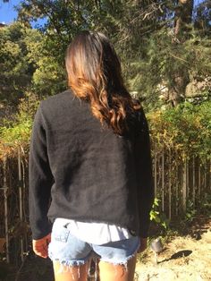 the back of a woman's body wearing shorts and a black sweater with trees in the background