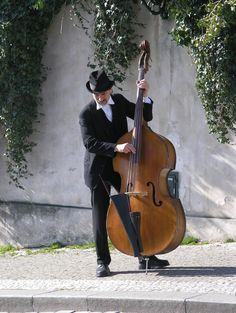 a man in a black suit and hat playing an instrument on the side of a road