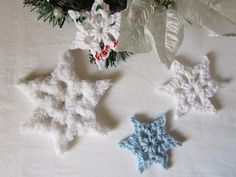 three crocheted snowflakes on a white tablecloth with pine branches in the background