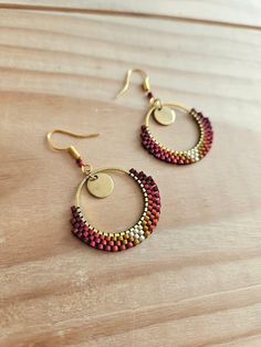 a pair of gold and red beaded hoop earrings on a wooden table with a wood surface