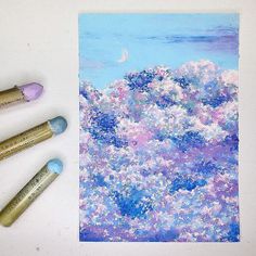 some paint brushes are sitting on a table next to an art work with blue and pink flowers