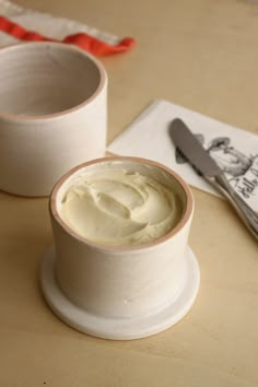 two white cups with cream sitting on top of a table next to a knife and napkin