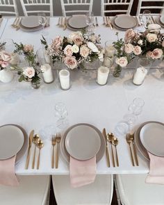 the table is set with pink and white flowers, silverware, and gold place settings