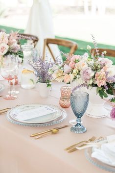 the table is set with pink and white flowers in vases, silverware, and plates