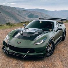 a green sports car parked on top of a dirt road next to mountains in the background