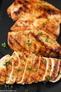 sliced chicken on a black plate with parsley and garlic sprinkled around the edges