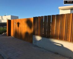 the shadow of a person standing in front of a wooden fence on a brick walkway