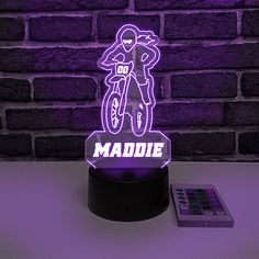 a purple light that says maddie on it next to a remote control and brick wall