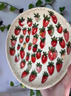 a hand holding a plate with strawberries painted on it