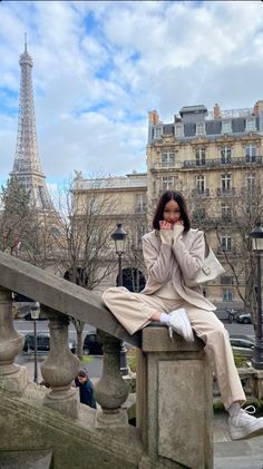 a woman is sitting on a ledge in front of the eiffel tower