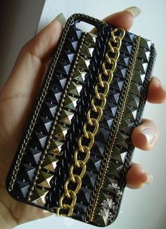 a hand holding a black and gold wallet with chains on it's sides,