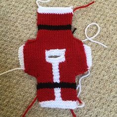 a knitted red vest sitting on top of a floor next to a pair of scissors